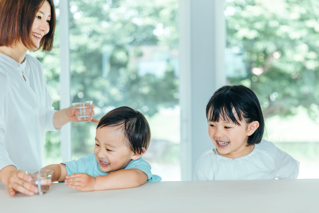 母親と幼い男の子と女の子が水の入ったガラスのコップを持ちながら笑っている様子