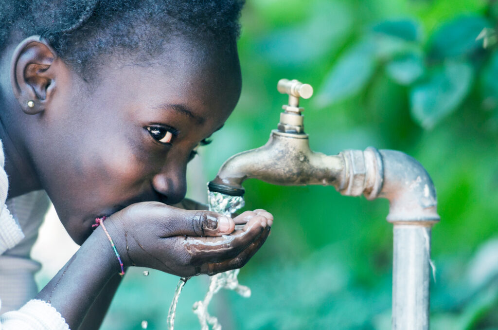 黒人のかわいい女の子が、蛇口からキレイな水を手で掬って嬉しそうに飲んでいる様子の画像