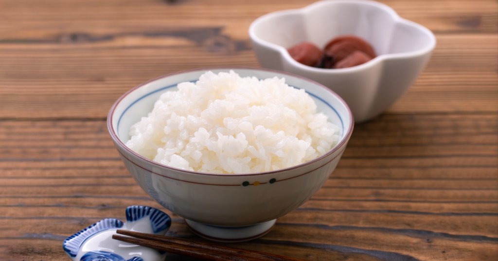 茶碗に盛られたお米と小鉢に入った梅干しが木の机に置かれている様子