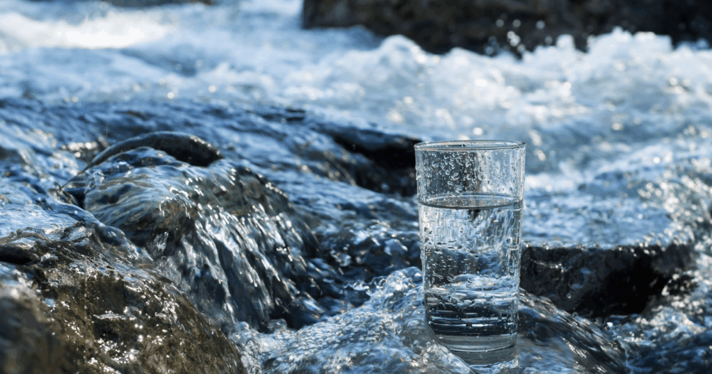川の中の岩に、水の入ったガラスのコップが置かれている様子