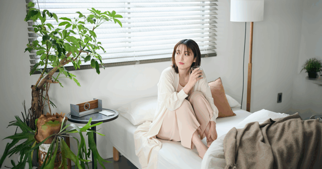 ベッドの上でガラスのコップに入った水を片手に持っている女性の写真