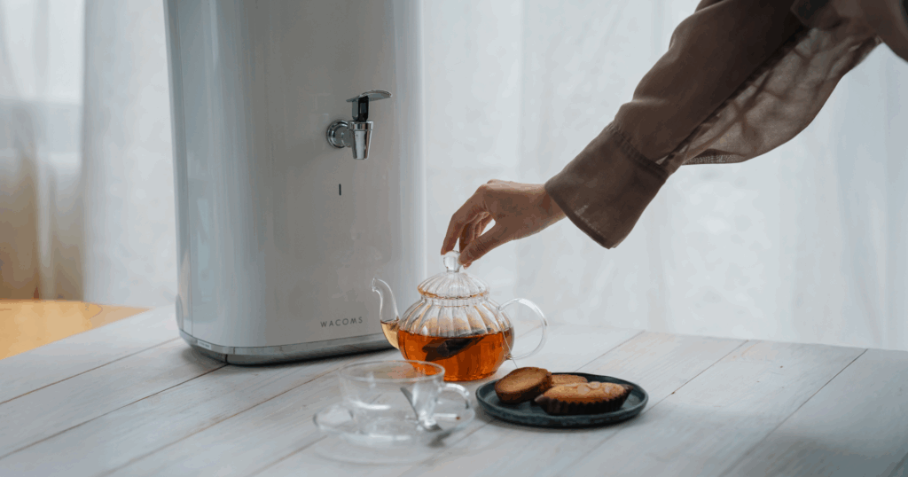 机の上に浄水器WACOMS TRUSTと紅茶の入ったティーポットと洋菓子が置いてある写真。