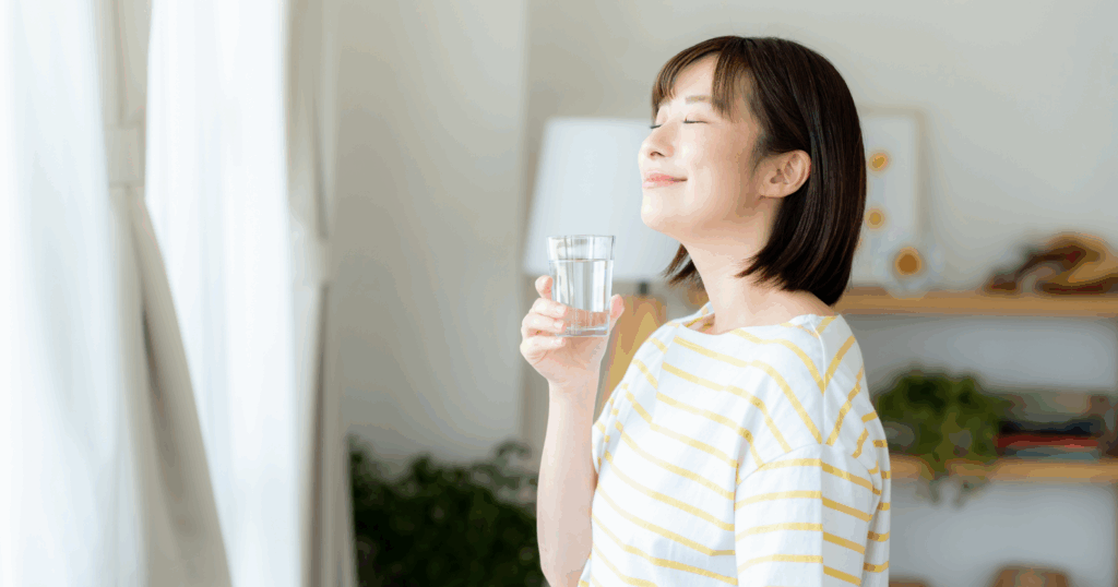 女性が朝日を浴びながらコップの水を持っている写真