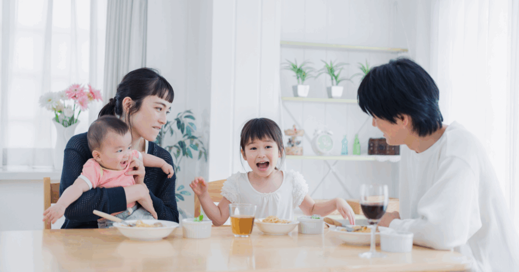 若い夫婦と子ども２人がリビングの机で食卓を囲む写真