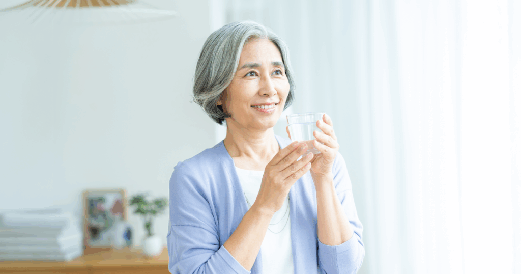 自宅でシルバーヘアの女性がガラスのコップに入った水を飲んでいる様子
