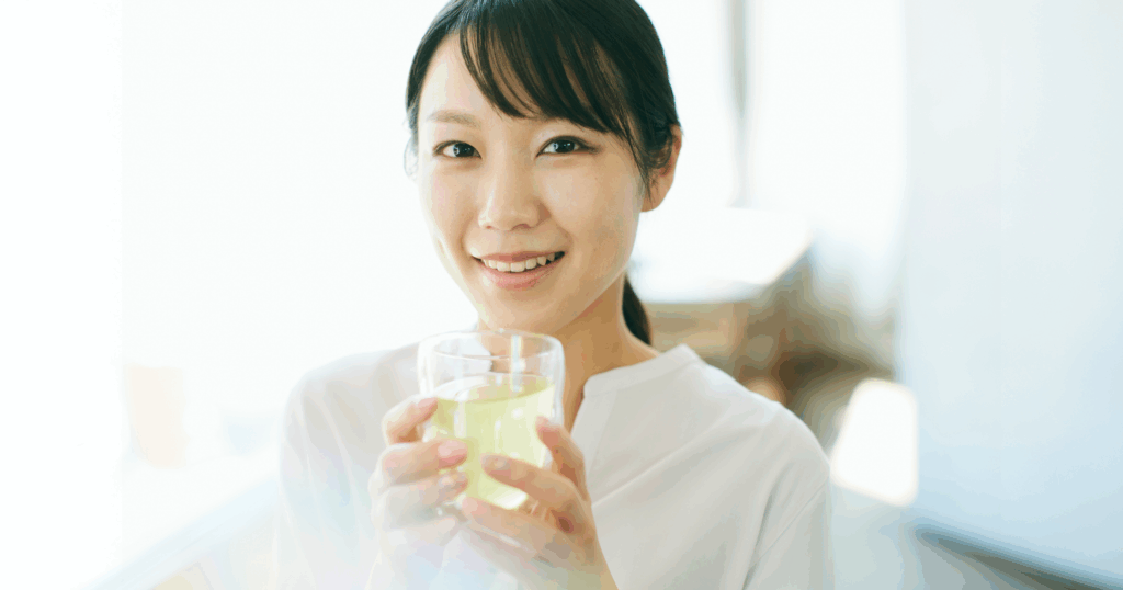 室内でガラスのコップに入った飲料を顔の前に持っている女性の画像