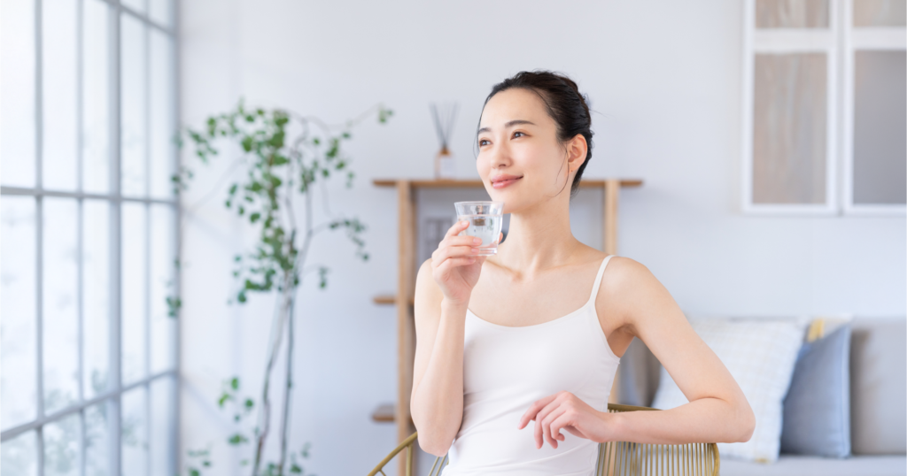 女性が窓際でガラスに入った水を飲んでいる様子
