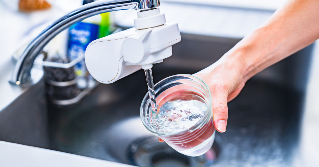 シンクに取り付けた蛇口取り付け型浄水器からガラスのコップに水を汲んでいる様子