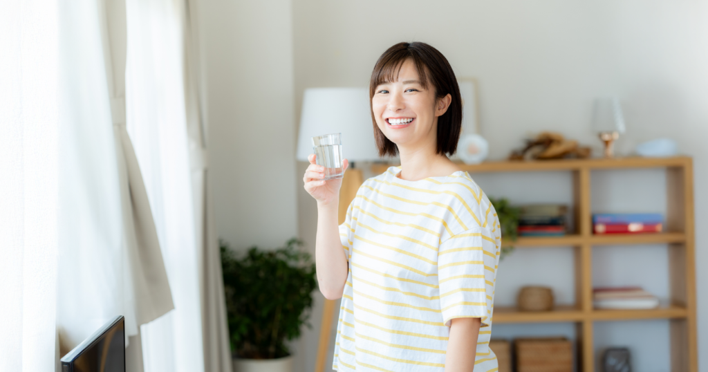 ガラスのコップに入った水を片手に微笑む女性