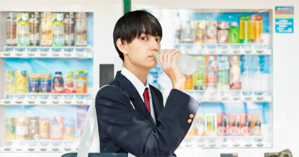 自動販売機の前で清涼飲料水を飲む男子学生