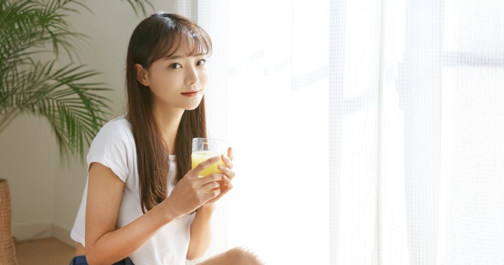 家の窓際でグラスに入ったオレンジジュースを持つ女性