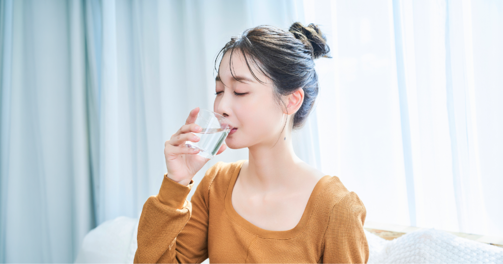 女性が家のソファでグラスに入った水を飲んでいる様子