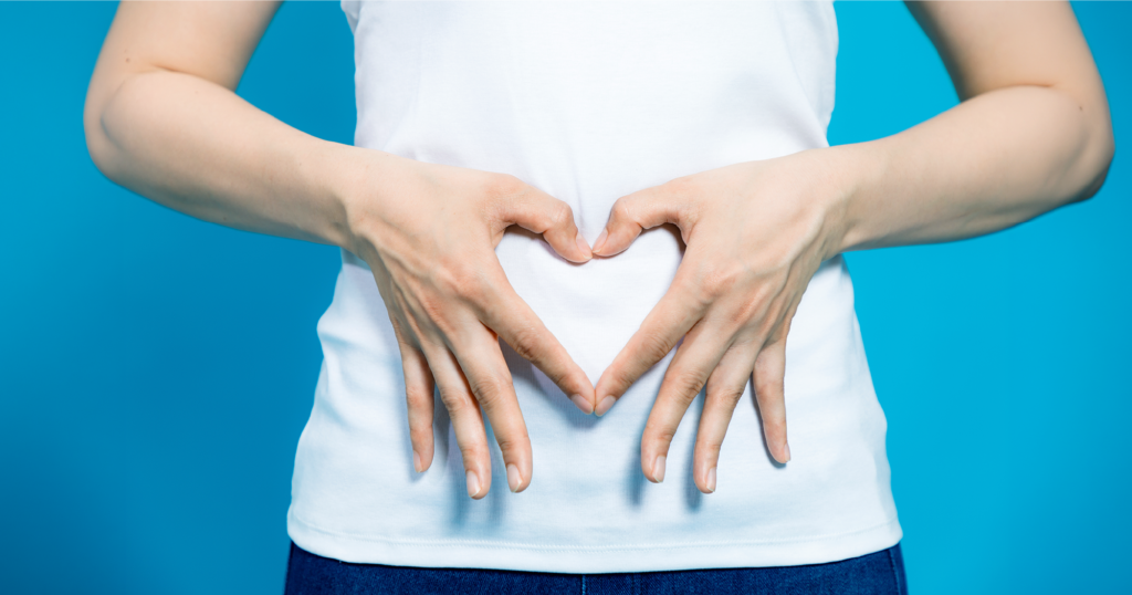 女性が指をハート型にした手をお腹にあてている写真。胃腸の健康のイメージ。