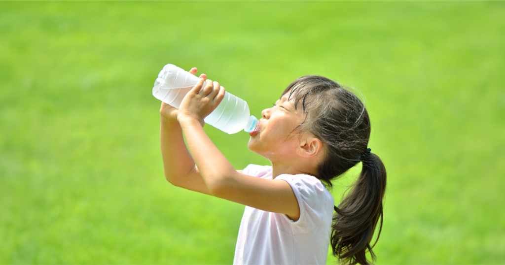 夏の草原で小さな女の子がペットボトルの水を飲んでいる様子