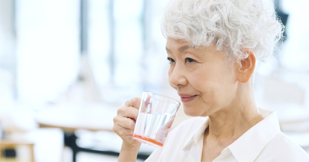 シニアの女性が透明のコップに入った水を飲む様子