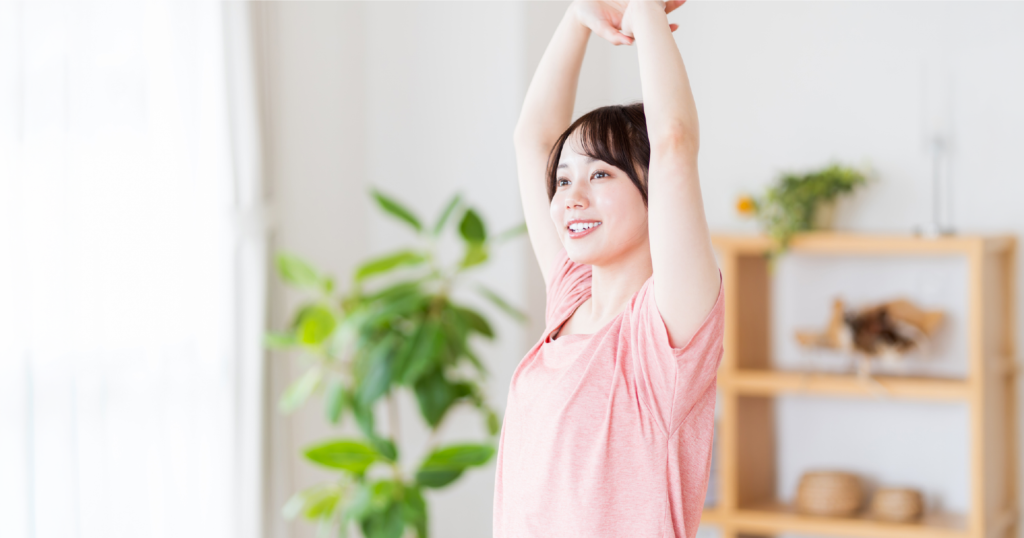 自宅で健康的な女性が両手を上に掲げ伸びのストレッチをしている様子