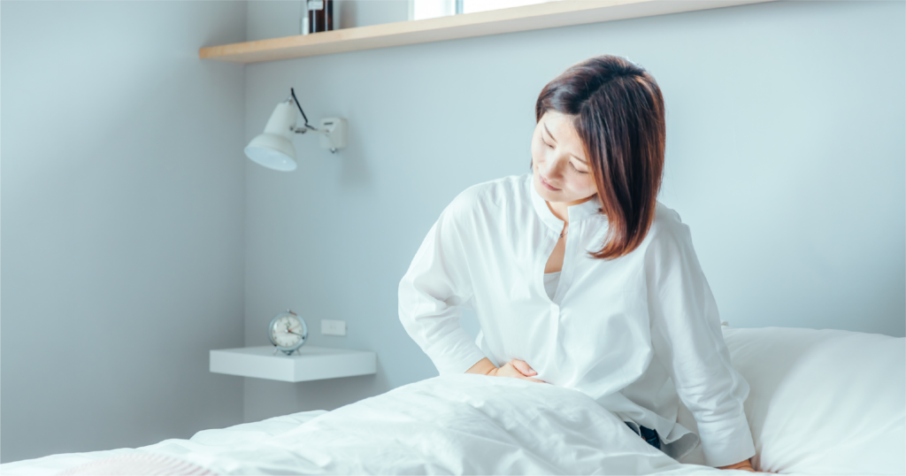 ベッドの上でお腹を抑えながら苦しむ女性。