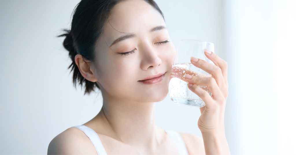 女性が自分の頬に、炭酸水の入ったガラスのコップを押し当てて、冷たくて気持ちいいという表情を浮かべている