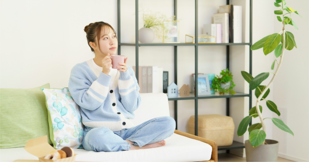 ソファの上でマグカップを両手で持ちリラックスする女性。