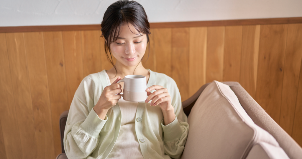 マグカップを持つ女性がソファに座っている様子。
