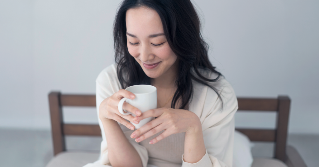 ベッドに座りマグカップで水分補給をしている女性。