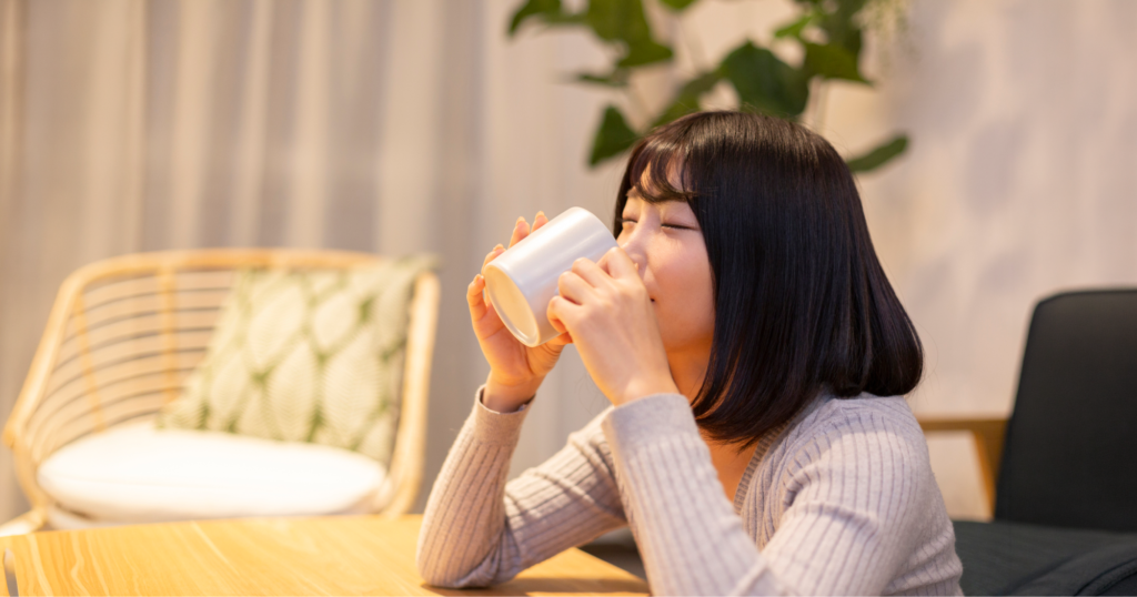 リビングに座りマグカップで水分補給をしている女性。