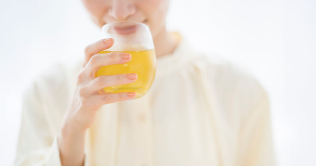 女性がガラスのコップで黄色い飲み物を飲んでいる様子