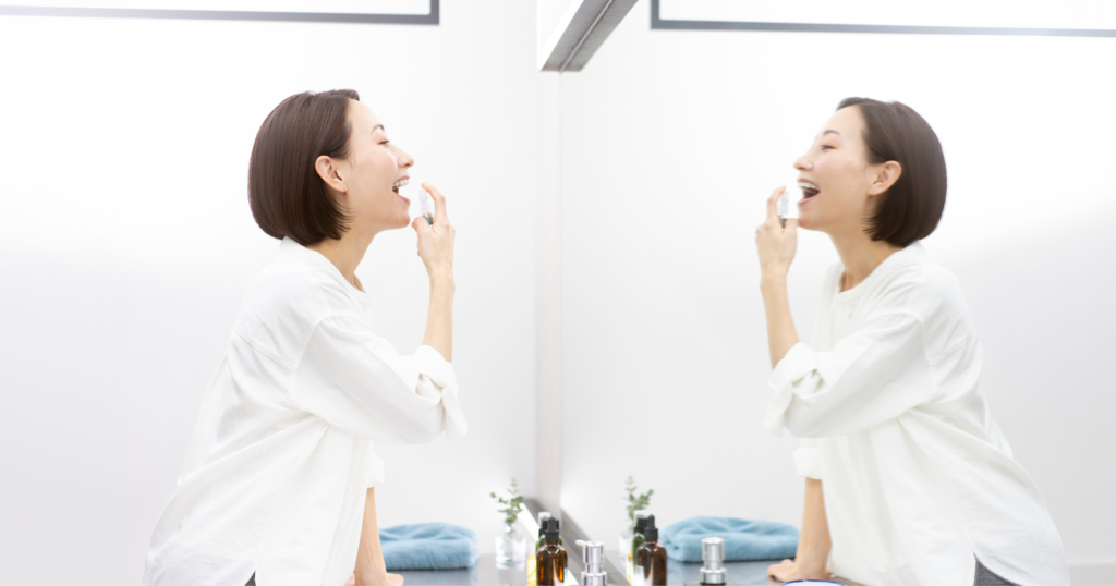 洗面所で鏡を見ながら喉にスプレーをかける女性
